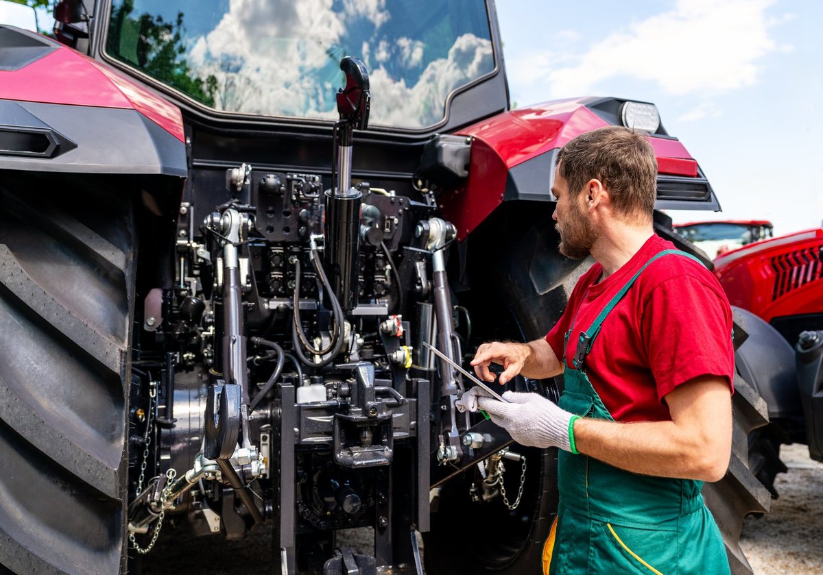 Technician checking farm tractor equipment in a rural field setting