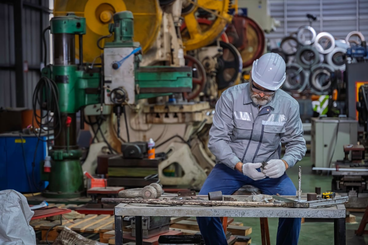 Factory technician inspecting formed metal components on a workbench in an industrial workshop